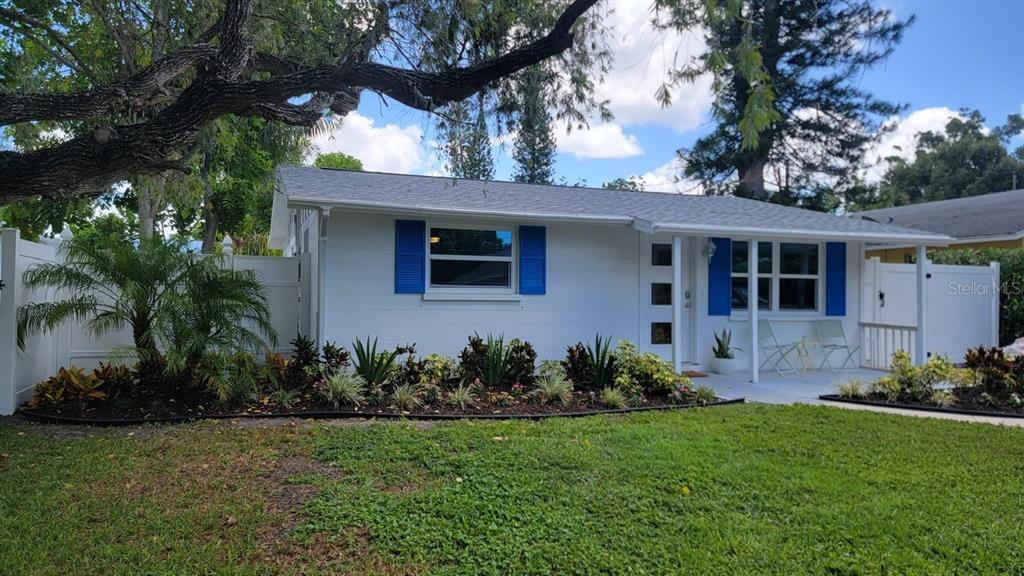 A white single-story house with blue shutters and a landscaped front yard under a tree — 3440 CHAPEL DRIVE, SARASOTA, FL