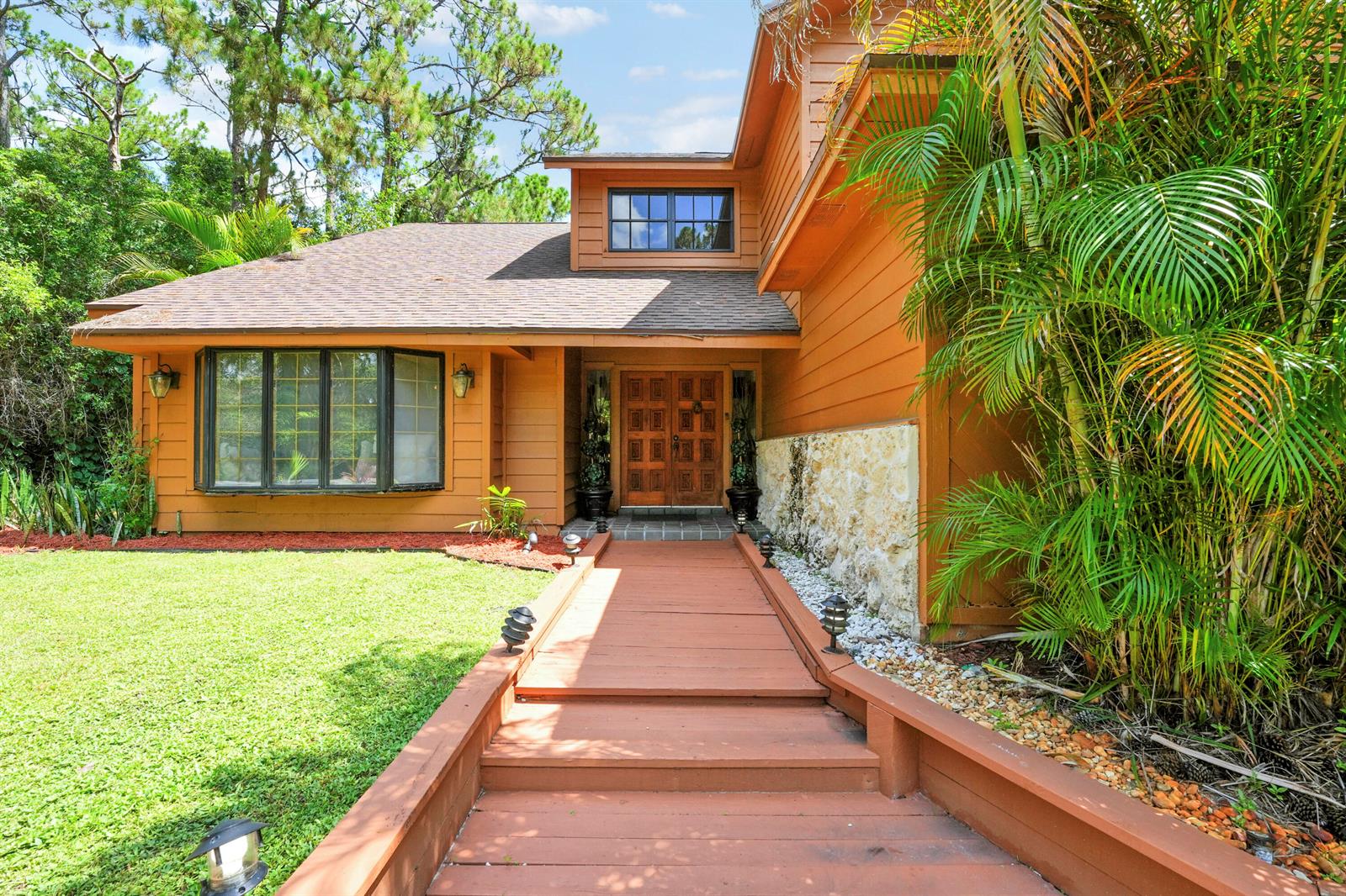 A wooden walkway leads to the front entrance of a two-story orange house — 12613 189th Court N, Jupiter FL 33478, JUPITER, FL