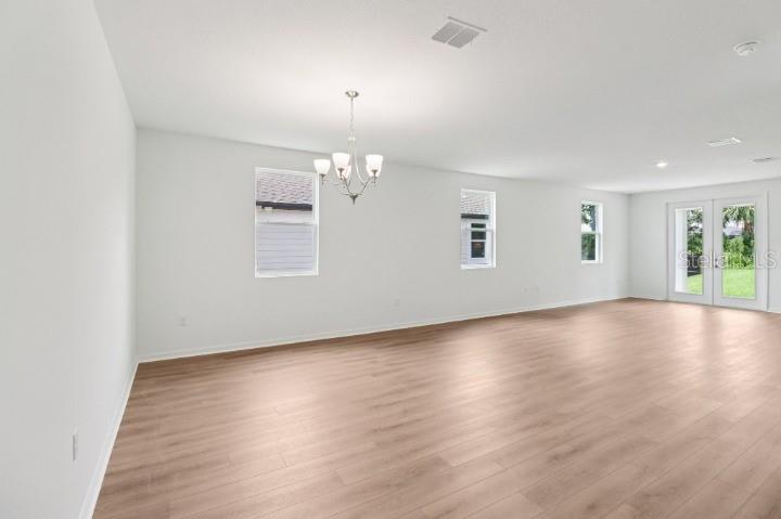 An empty room with light wood-look flooring, white walls, a chandelier, and glass patio doors — 17637 LAKE STAR ROAD, WINTER GARDEN, FL