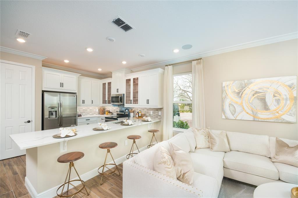 A kitchen with white cabinets and a breakfast bar overlooks a living area with seating — 32464 SEA LOCH LOOP, MOUNT DORA, FL