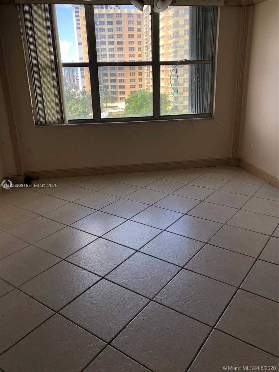 An empty room features light-colored tile flooring, beige walls, and a large window overlooking buildings — 2751 S Ocean Dr # 701N, Hollywood FL 33019, HOLLYWOOD, FL