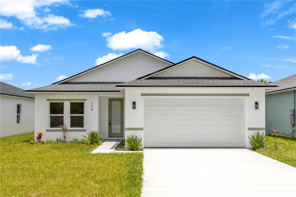 A single-story house with white stucco walls, a two-car garage, and a green front door — 136 11TH AVENUE, OSTEEN, FL