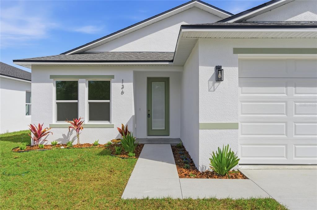 A white house exterior features a green front door, a garage, and a concrete walkway — 136 11TH AVENUE, OSTEEN, FL