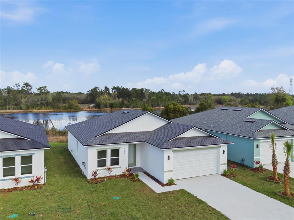 An aerial view shows a white single-story house with a two-car garage near water — 136 11TH AVENUE, OSTEEN, FL