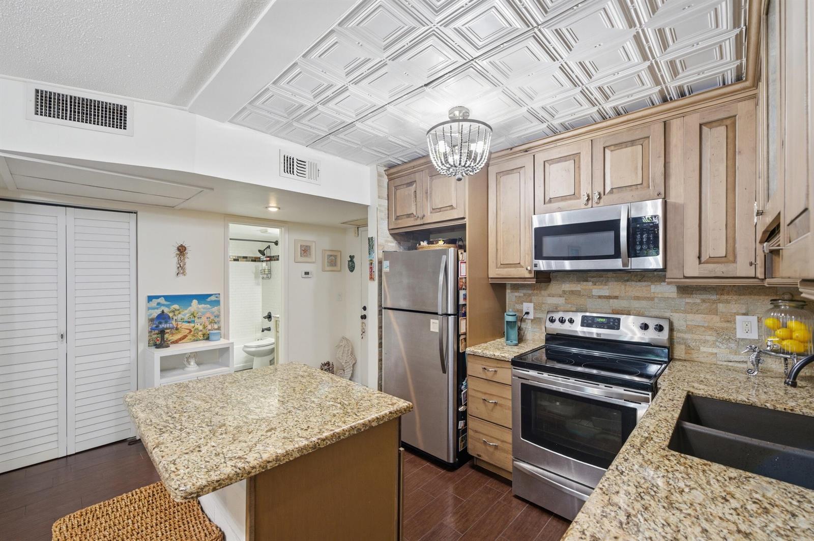A kitchen features granite countertops, stainless steel appliances, wood cabinets, and a decorative ceiling — 101 E Mcnab Road # 102, Pompano Beach FL 33060, POMPANO BEACH, FL