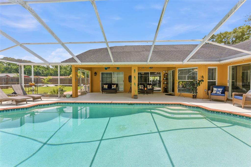 A swimming pool sits in front of a covered patio with outdoor furniture and screens — 19906 JODI DRIVE, LUTZ, FL