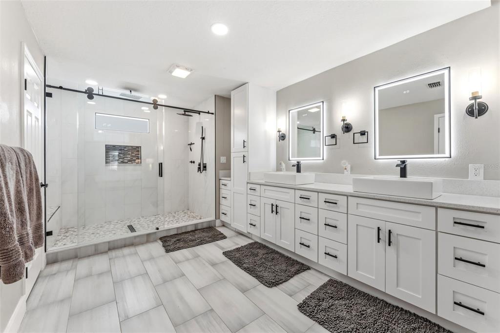 A modern bathroom features a glass-enclosed walk-in shower, double vanity, and light-colored tile flooring — 19906 JODI DRIVE, LUTZ, FL