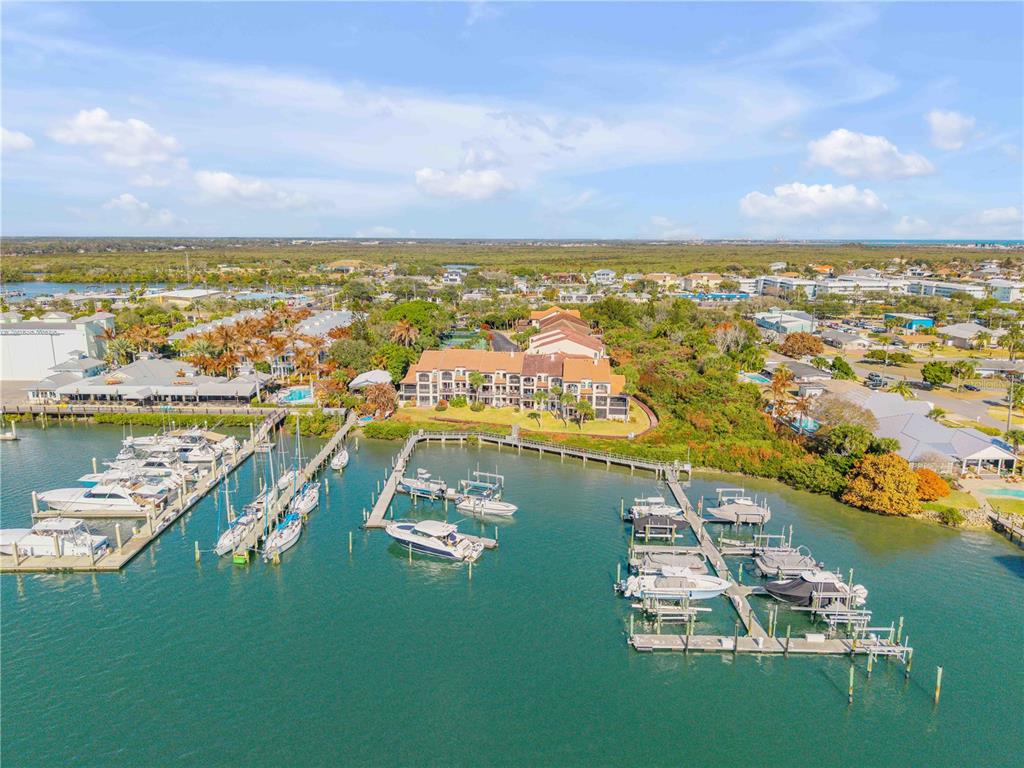 An aerial view shows a multi-story waterfront condominium complex with private boat docks and slips — 135 MARINA BAY DRIVE, NEW SMYRNA BEACH, FL