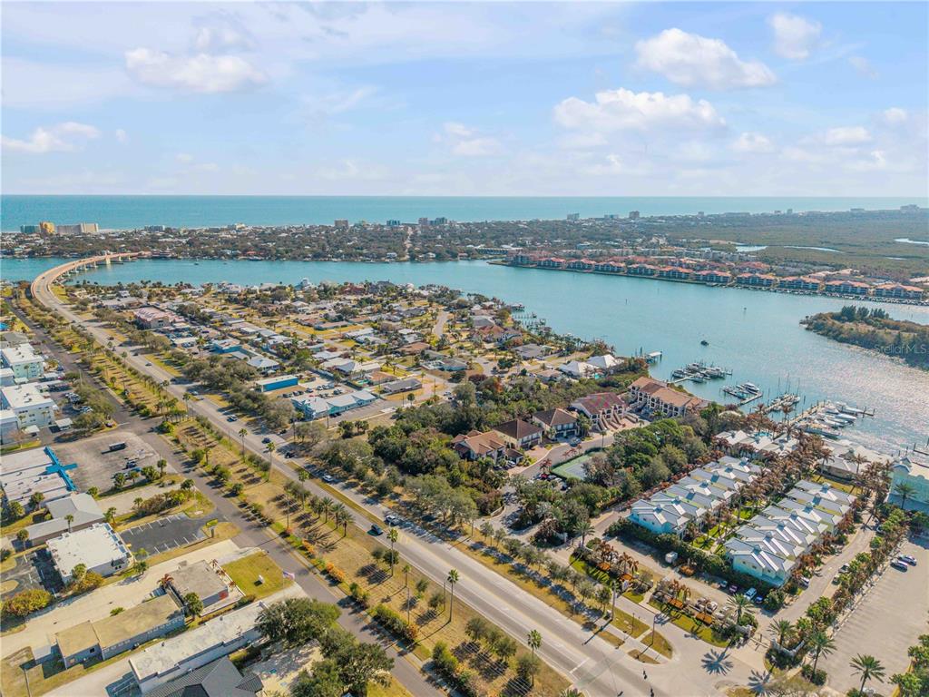 An aerial view shows a coastal neighborhood with a bridge, marina, and the ocean beyond — 135 MARINA BAY DRIVE, NEW SMYRNA BEACH, FL