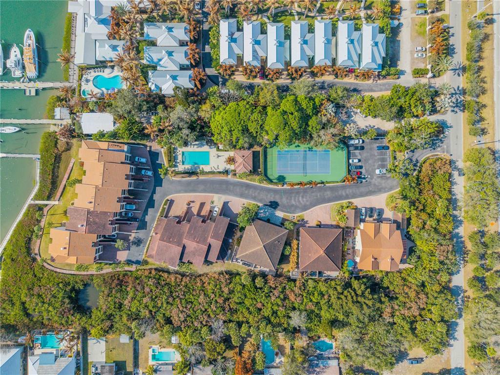 An aerial view shows a residential complex with a tennis court, swimming pools, and docks — 135 MARINA BAY DRIVE, NEW SMYRNA BEACH, FL