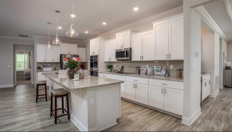 A kitchen features white cabinets, granite countertops, a center island with stools, and wood flooring — 49 VINCA STREET, HOMOSASSA, FL