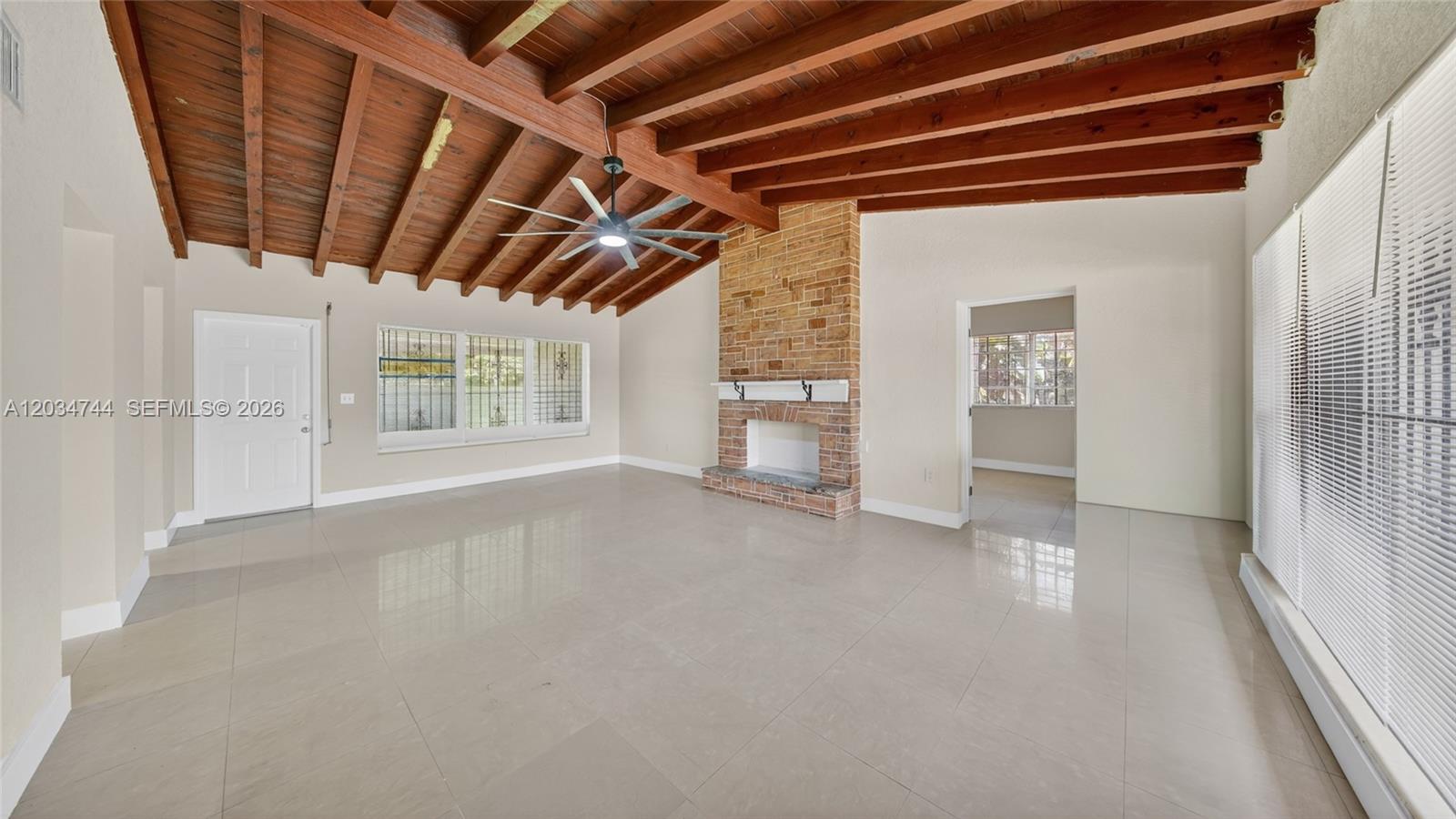 A living room features a vaulted wood-beamed ceiling, tile flooring, and a brick fireplace — 8200 NW 34th Ave, Miami FL 33147, MIAMI, FL