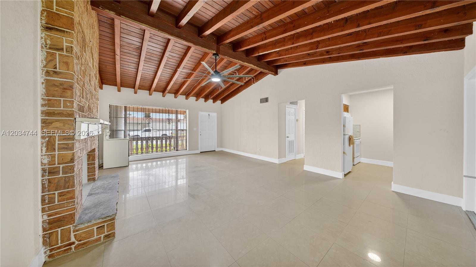 A living room features a brick fireplace, vaulted wood-beam ceiling, and light-colored tile flooring — 8200 NW 34th Ave, Miami FL 33147, MIAMI, FL