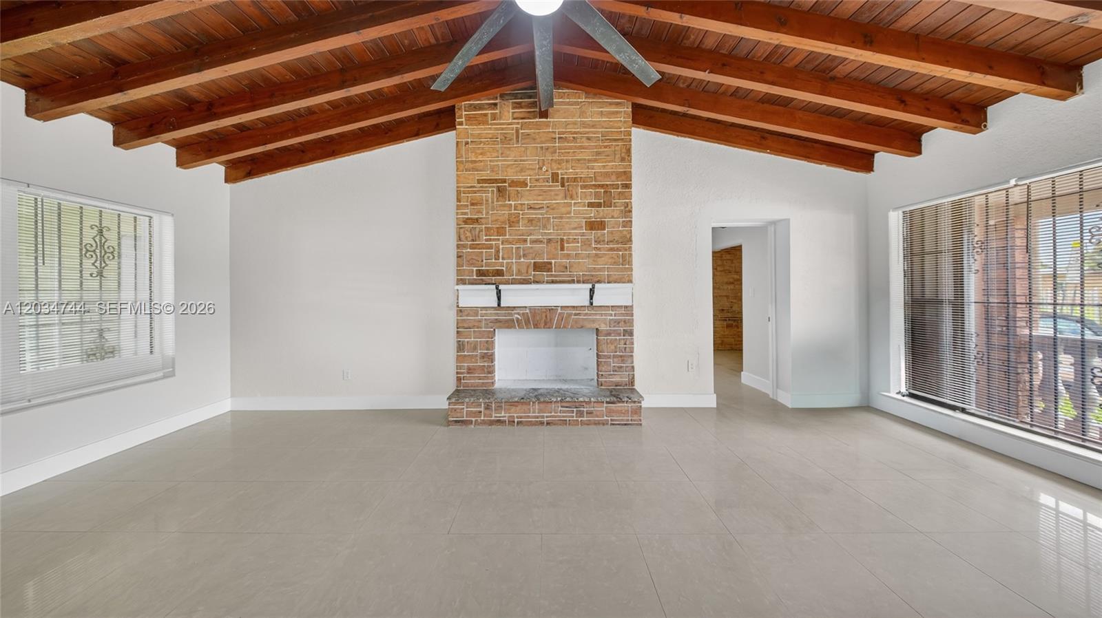 A living room features a brick fireplace, vaulted wood-beamed ceiling, and light-colored tile flooring — 8200 NW 34th Ave, Miami FL 33147, MIAMI, FL