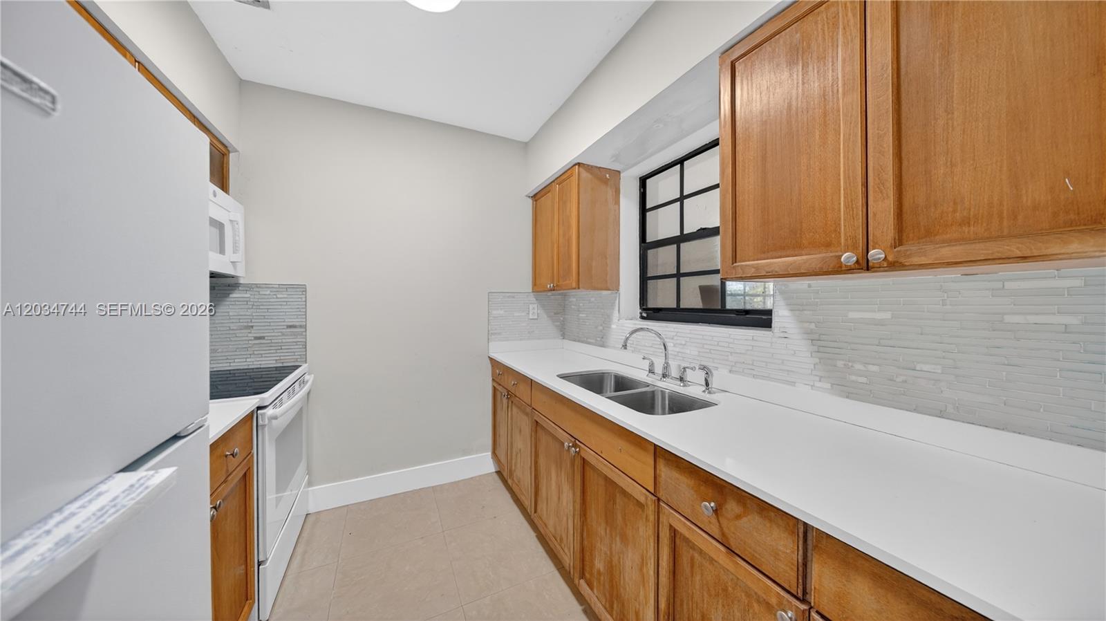 A kitchen features wooden cabinets, white countertops, a double sink, and a white refrigerator — 8200 NW 34th Ave, Miami FL 33147, MIAMI, FL
