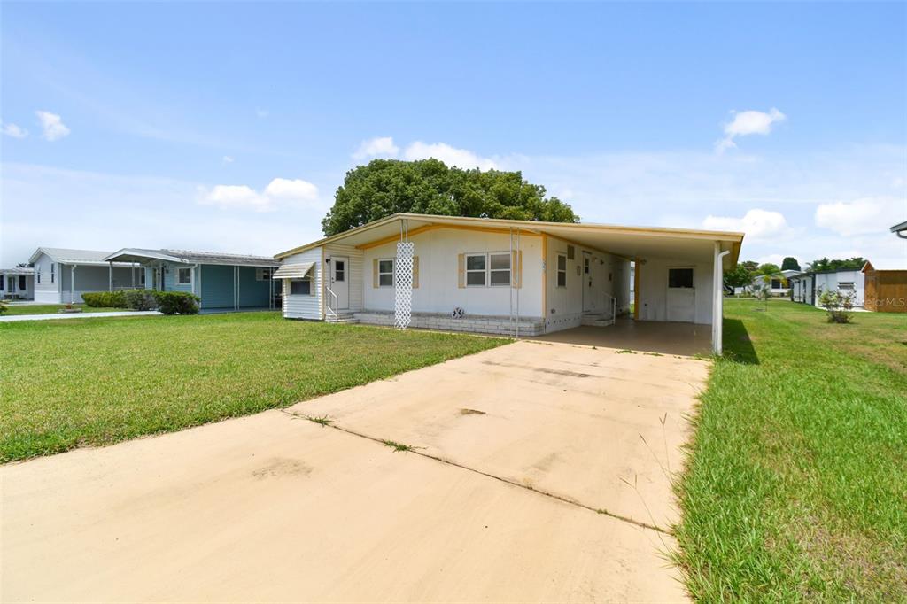 A single-story mobile home with a concrete driveway and an attached carport under a blue sky — 5353 COMANCHE STREET, ZEPHYRHILLS, FL