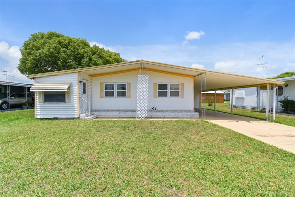A single-story manufactured home with a white exterior, a front porch, and an attached carport — 5353 COMANCHE STREET, ZEPHYRHILLS, FL