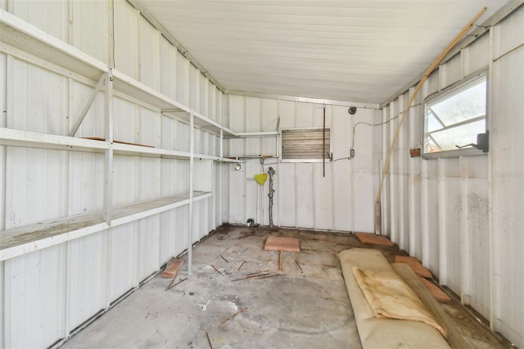An interior view of a shed with metal walls, built-in shelving, and a concrete floor — 5353 COMANCHE STREET, ZEPHYRHILLS, FL