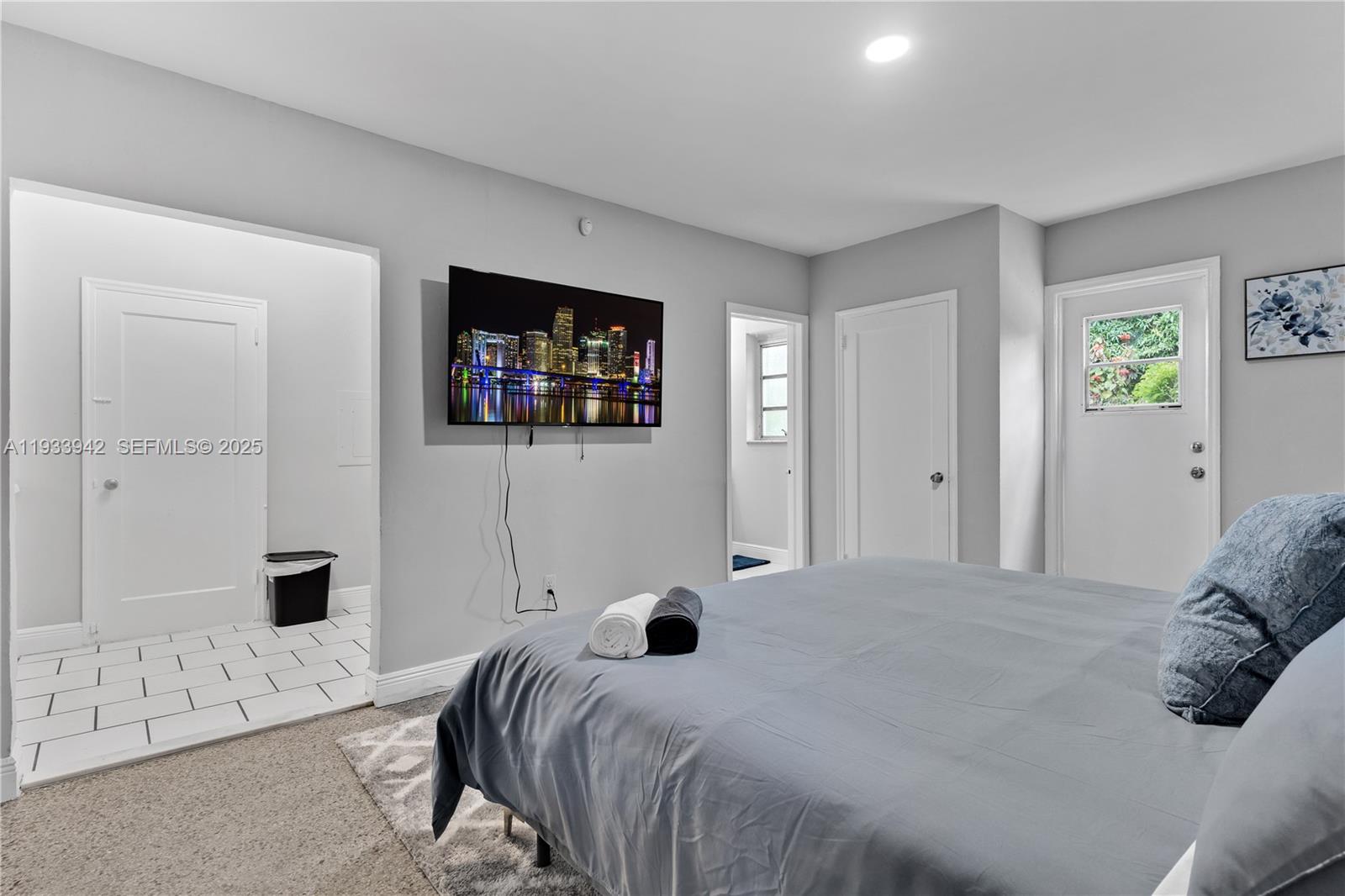 A bedroom features a bed, a wall-mounted television, and multiple doorways leading to other rooms — 427 NE 107th St # 2, Miami FL 33161, MIAMI, FL