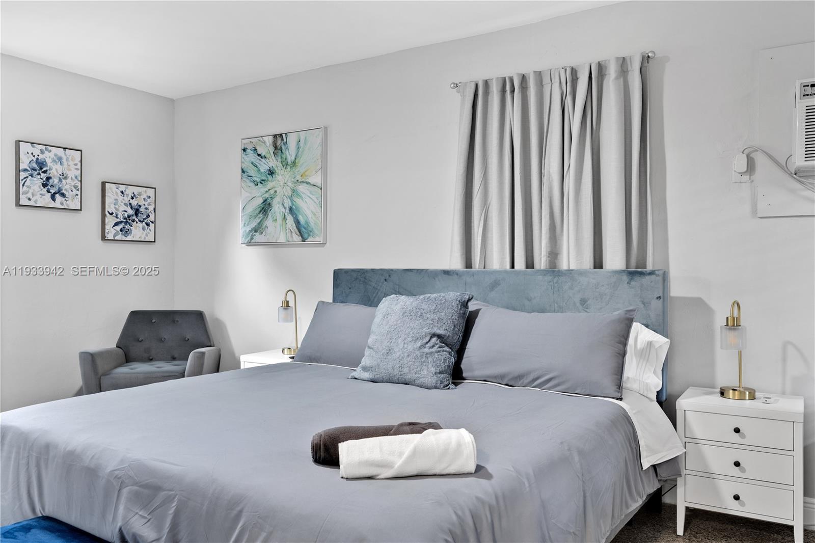 A bedroom features a gray bed, two white nightstands, and wall art on a light wall — 427 NE 107th St # 2, Miami FL 33161, MIAMI, FL