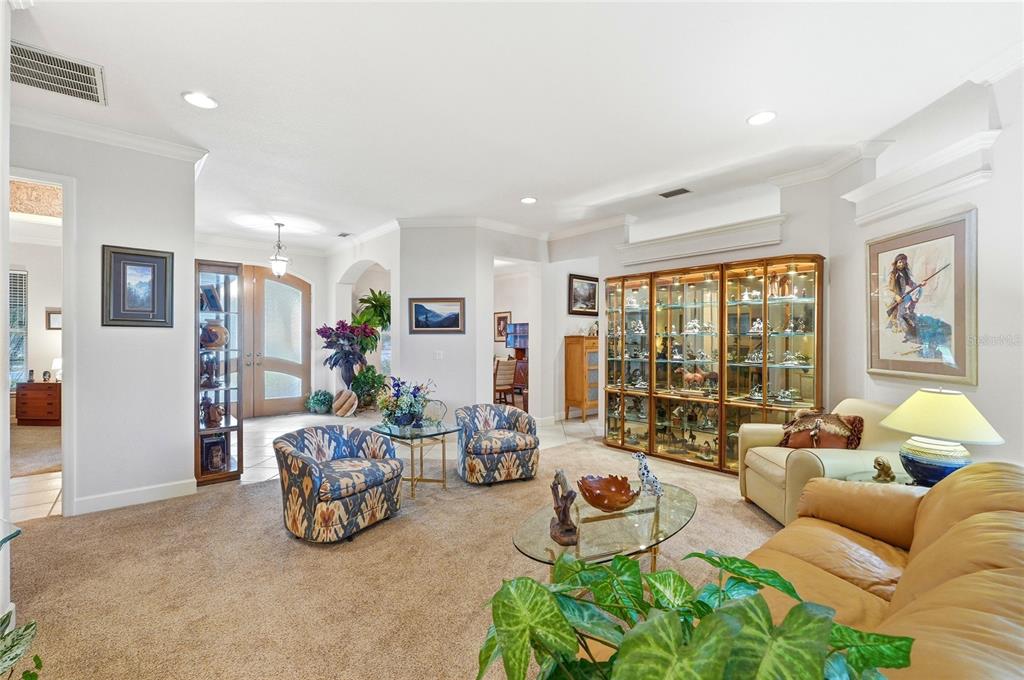 A living room features carpeted flooring, a large glass display cabinet, and patterned armchairs — 108 LAKE REGION BOULEVARD N, WINTER HAVEN, FL