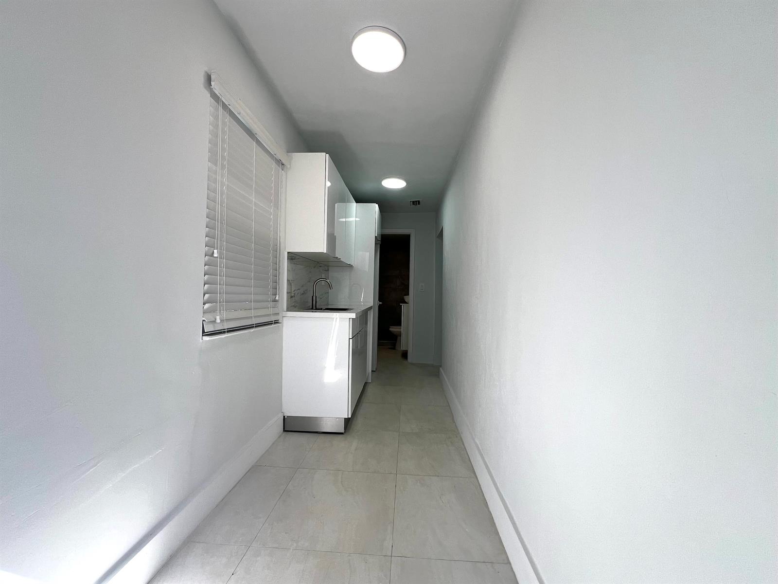 A narrow, white-walled kitchenette features glossy cabinets, a sink, and light-colored tile flooring — 10730 SW 149th Terrace, Miami FL 33176, MIAMI, FL