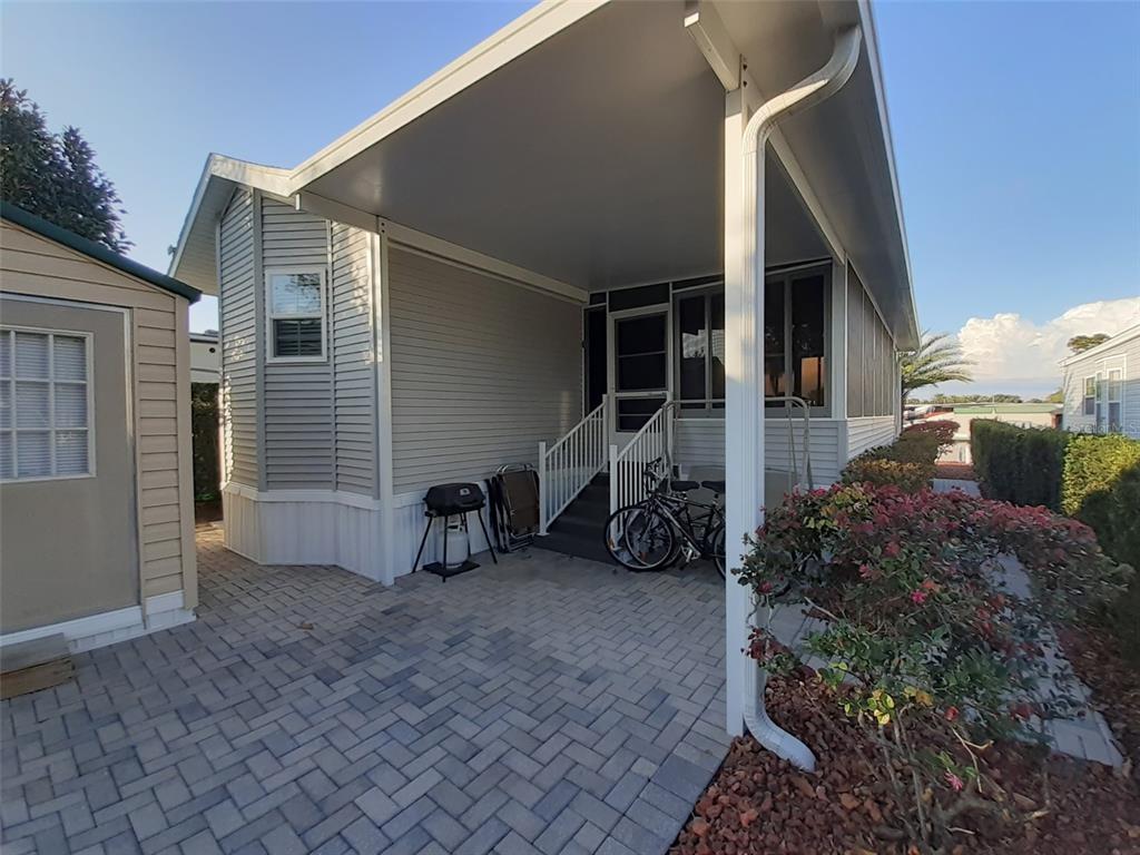 A paved patio sits beneath a carport next to a light-gray mobile home — 2330 LIMEWOOD AVENUE UNIT 051, CLERMONT, FL