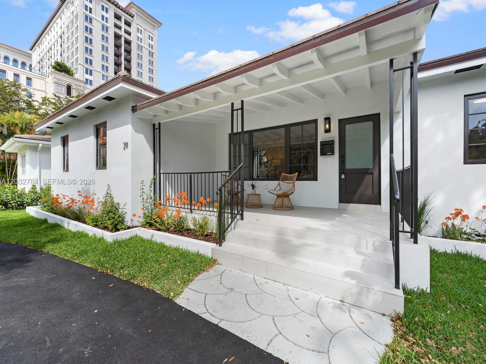 A white house exterior features a covered porch with black railings and a stone walkway — 39 Palermo Ave, Coral Gables FL 33134, CORAL GABLES, FL