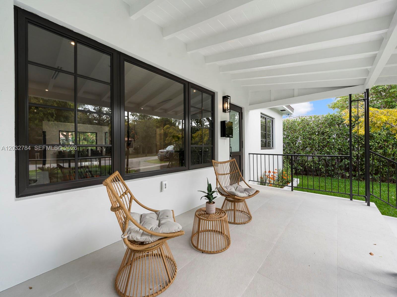 A covered patio features two wicker chairs, a small side table, and large dark-framed windows — 39 Palermo Ave, Coral Gables FL 33134, CORAL GABLES, FL