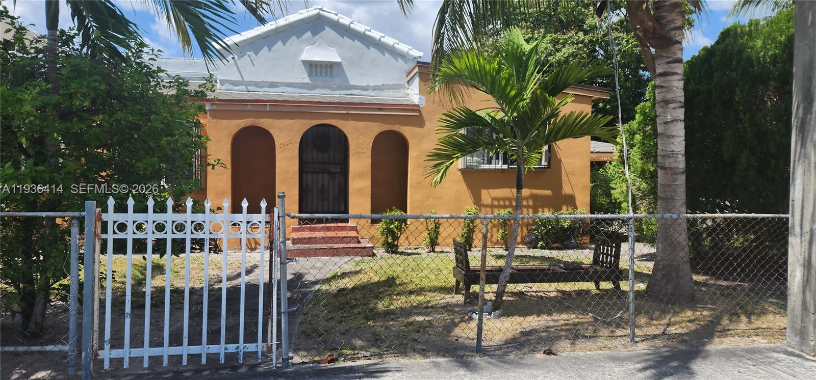 A single-story orange house features a central arched entryway and a white metal fence — 5428 NW 13th Ave, Miami FL 33142, MIAMI, FL