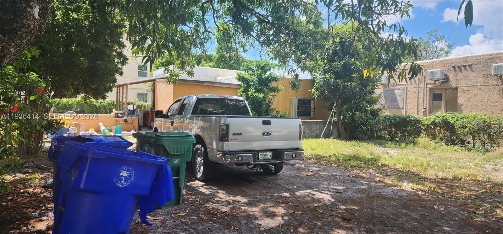 A silver pickup truck is parked on a dirt lot next to blue and green trash bins — 5428 NW 13th Ave, Miami FL 33142, MIAMI, FL