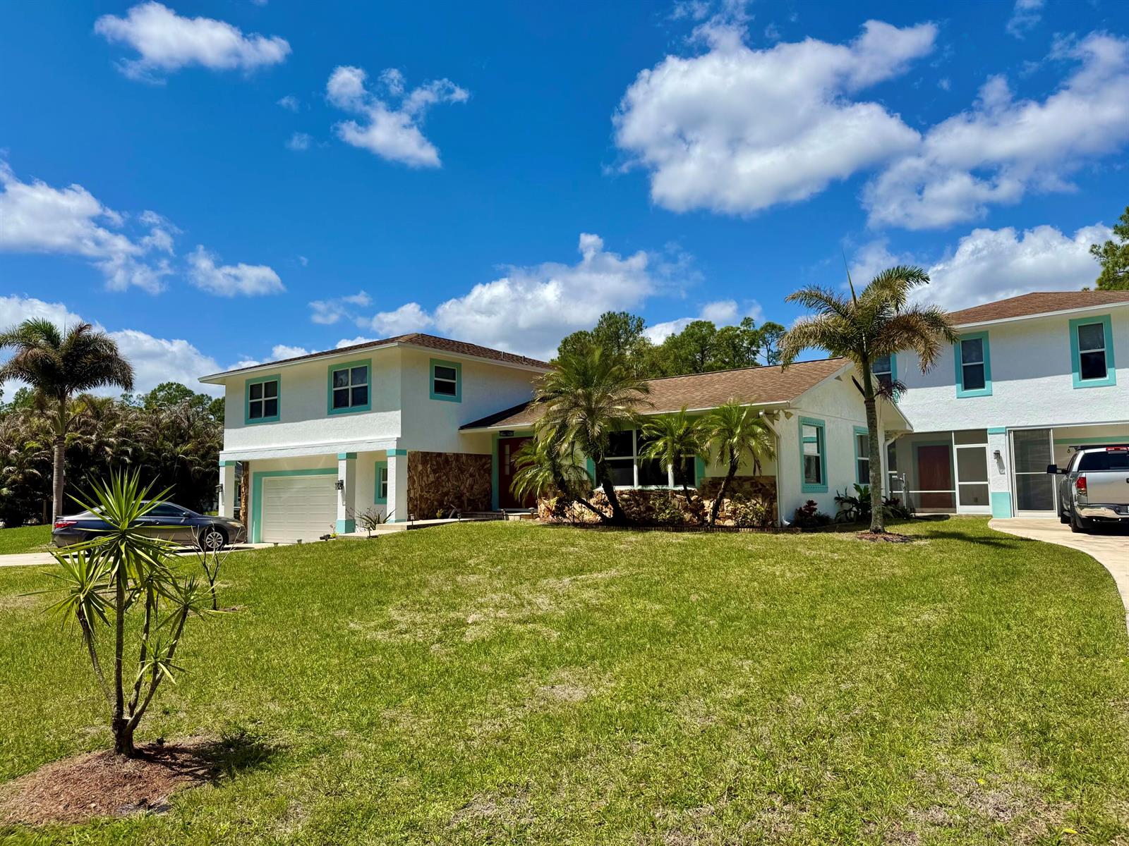 A two-story house with white stucco, turquoise trim, and stone accents under a blue sky — 16283 Alexander Run, Jupiter FL 33478, JUPITER, FL