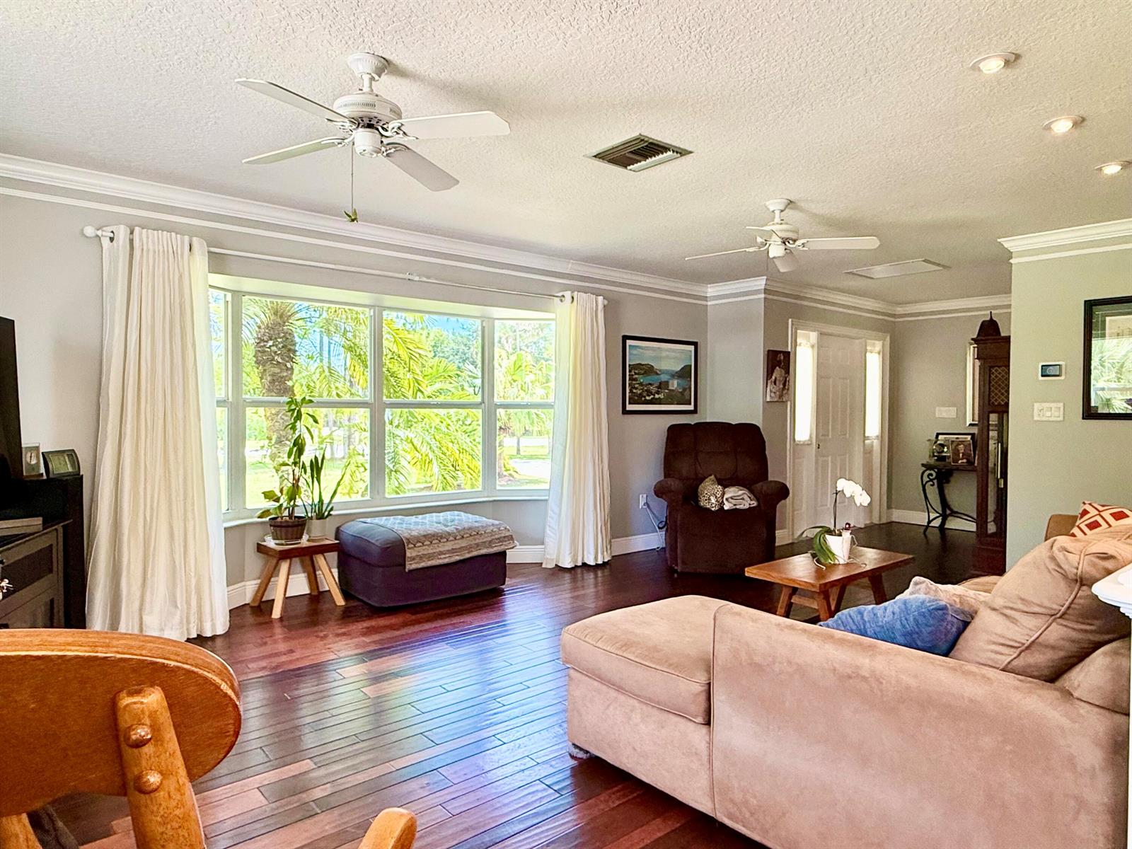 A living room features dark wood floors, a bay window, two ceiling fans, and furniture — 16283 Alexander Run, Jupiter FL 33478, JUPITER, FL