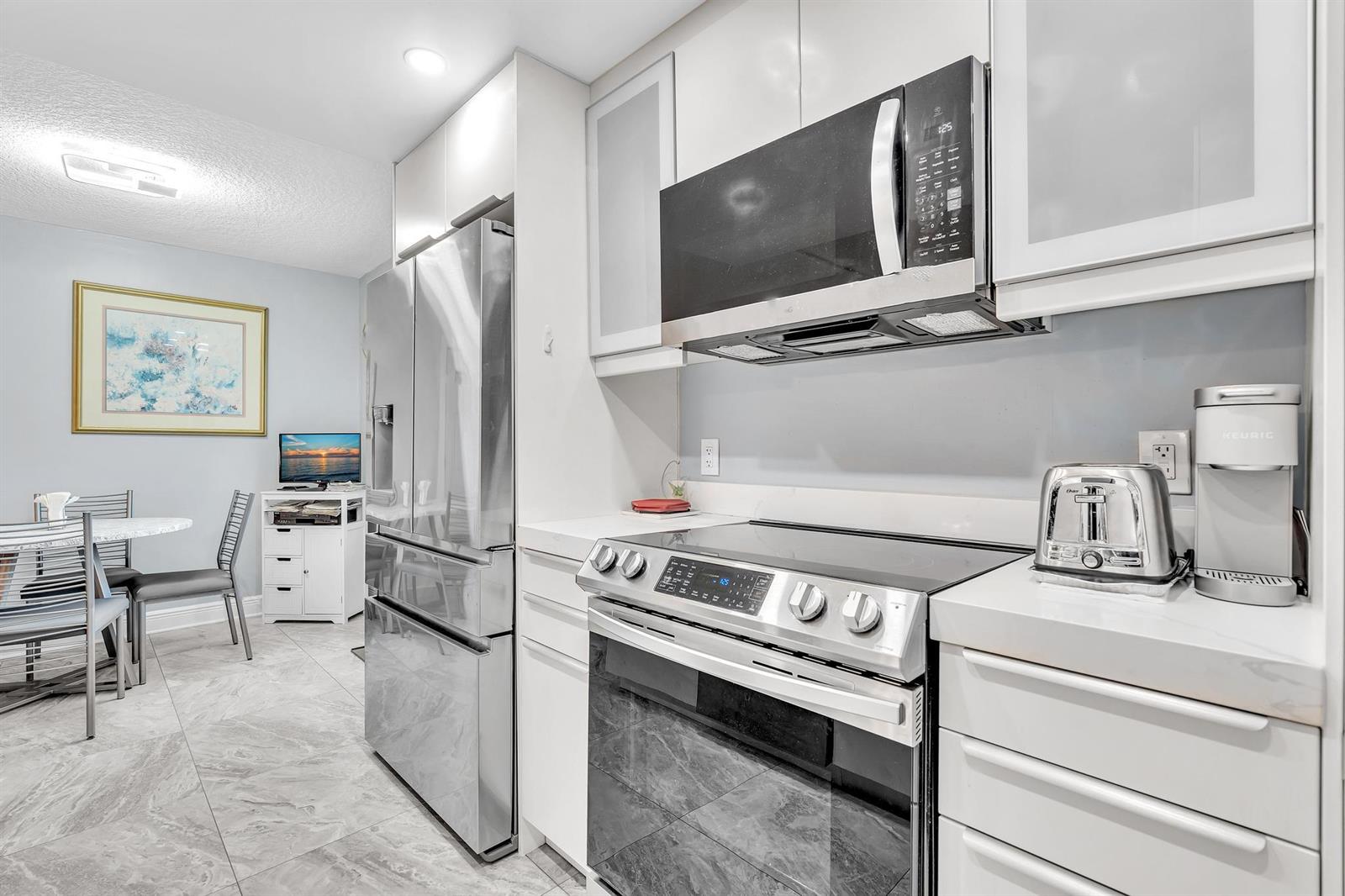 A modern kitchen features stainless steel appliances, white cabinetry, and light gray tile flooring — 625 Normandy N # 625, Delray Beach FL 33484, DELRAY BEACH, FL