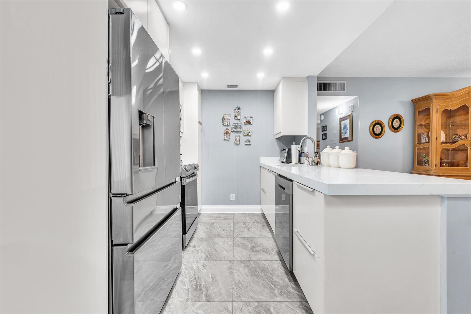 A modern kitchen features stainless steel appliances, white cabinetry, and gray marble-patterned tile flooring — 625 Normandy N # 625, Delray Beach FL 33484, DELRAY BEACH, FL