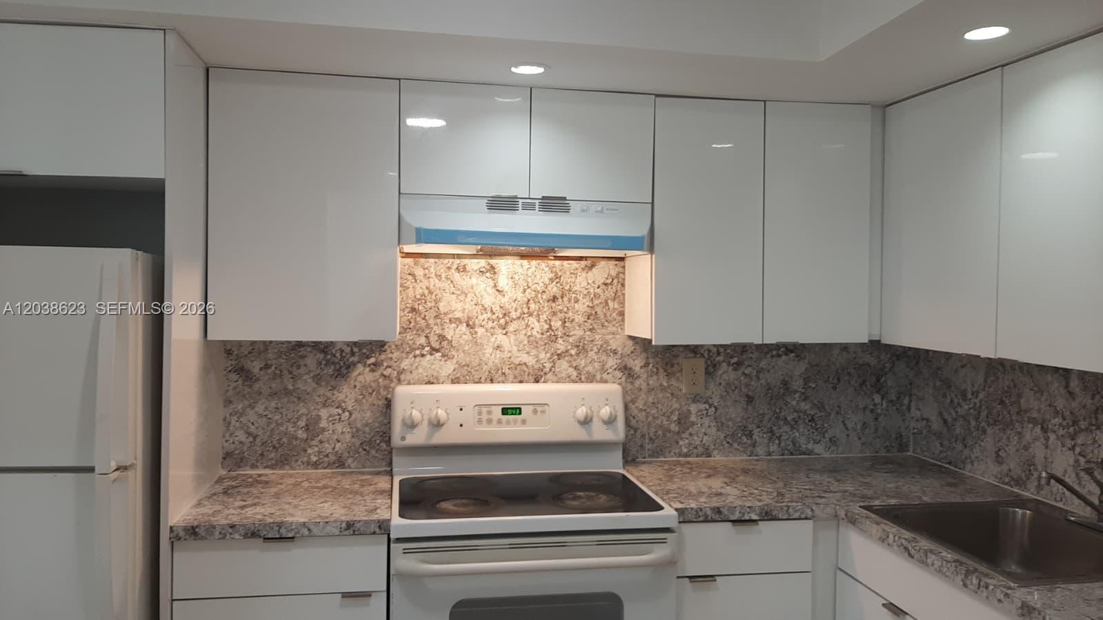 A kitchen features white cabinets, a white electric stove, and a speckled gray stone backsplash — 1750 NE 191st St # 2, Miami FL 33179, MIAMI, FL