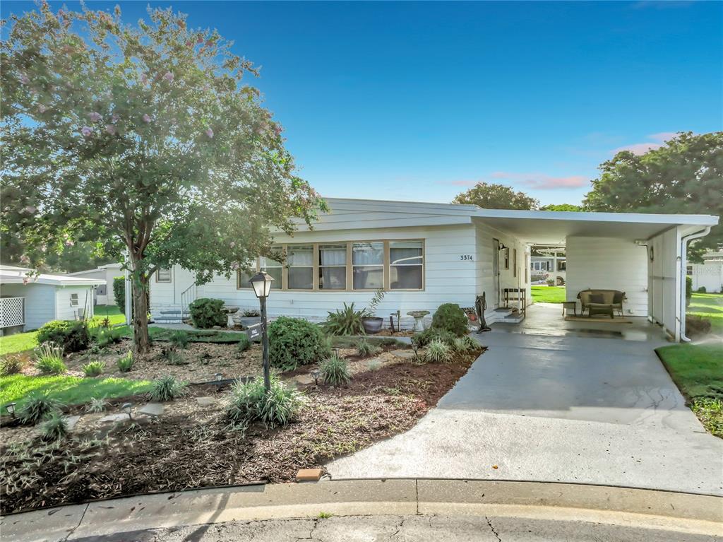 A white single-story manufactured home features a large carport, a landscaped front yard, and trees — 3374 EVERGREEN ROAD UNIT 1700, ZELLWOOD, FL