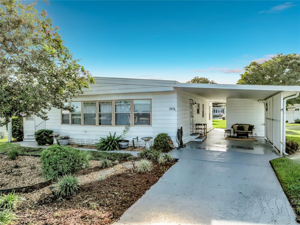 A white mobile home features a front carport, a landscaped yard, and a concrete driveway — 3374 EVERGREEN ROAD UNIT 1700, ZELLWOOD, FL