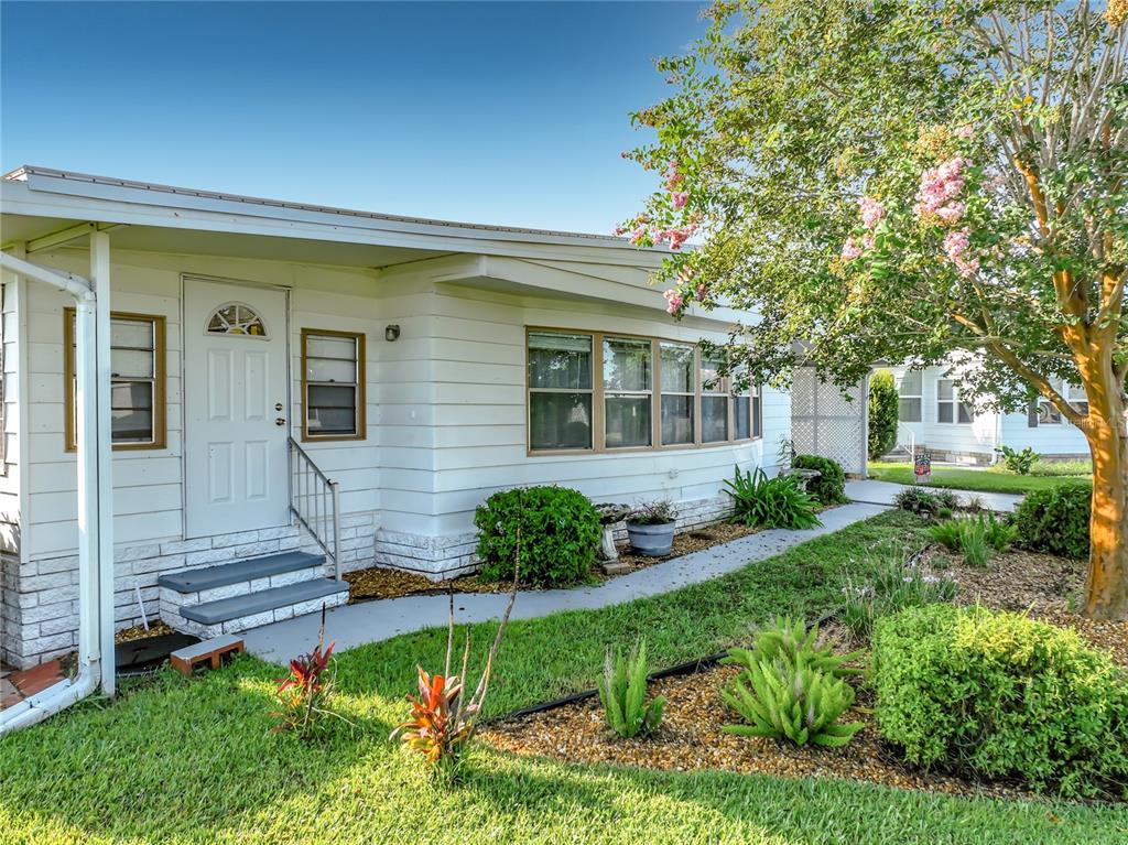A white mobile home with a front door, steps, and a landscaped yard with trees — 3374 EVERGREEN ROAD UNIT 1700, ZELLWOOD, FL