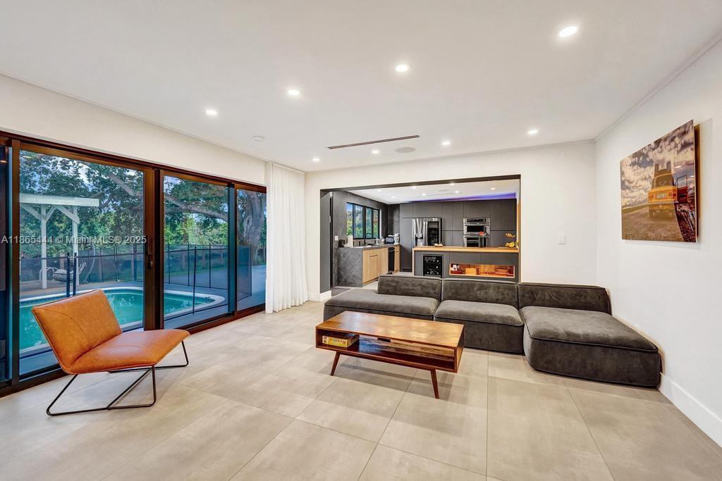 A modern living room with large sliding glass doors, a grey sectional, and an open kitchen — 4660 SW 37th Ave, Dania Beach FL 33312, DANIA BEACH, FL