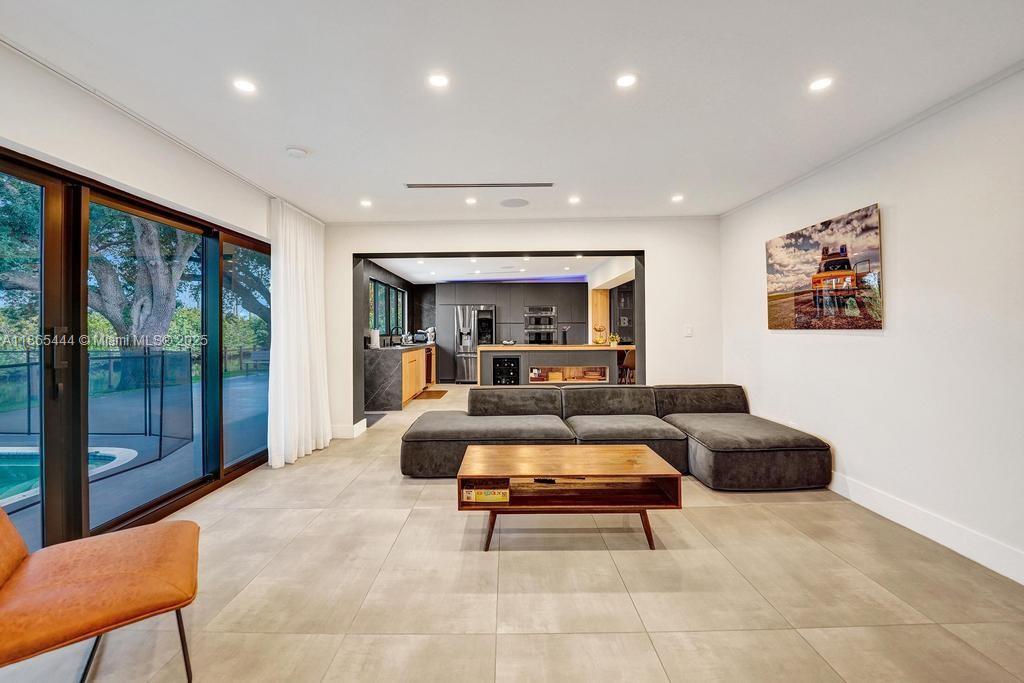 A modern living room with large sliding glass doors, a grey sectional, and an open kitchen — 4660 SW 37th Ave, Dania Beach FL 33312, DANIA BEACH, FL