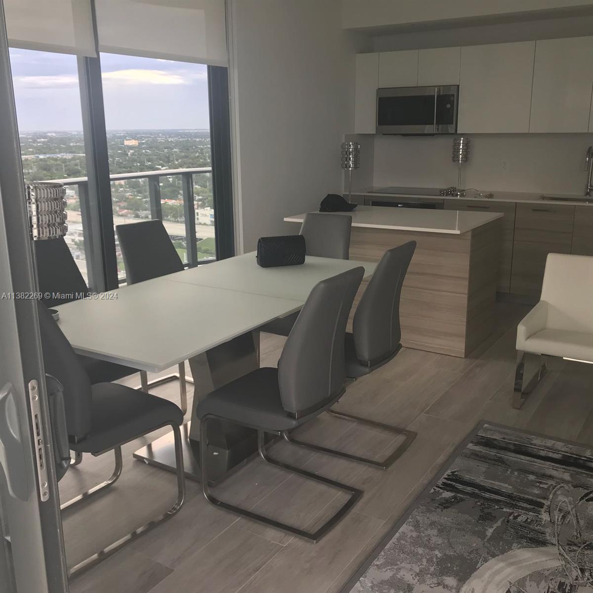 A modern dining area features a white table, gray chairs, and an adjacent kitchen island — 121 NE 34th St # 2601, Miami FL 33137, MIAMI, FL