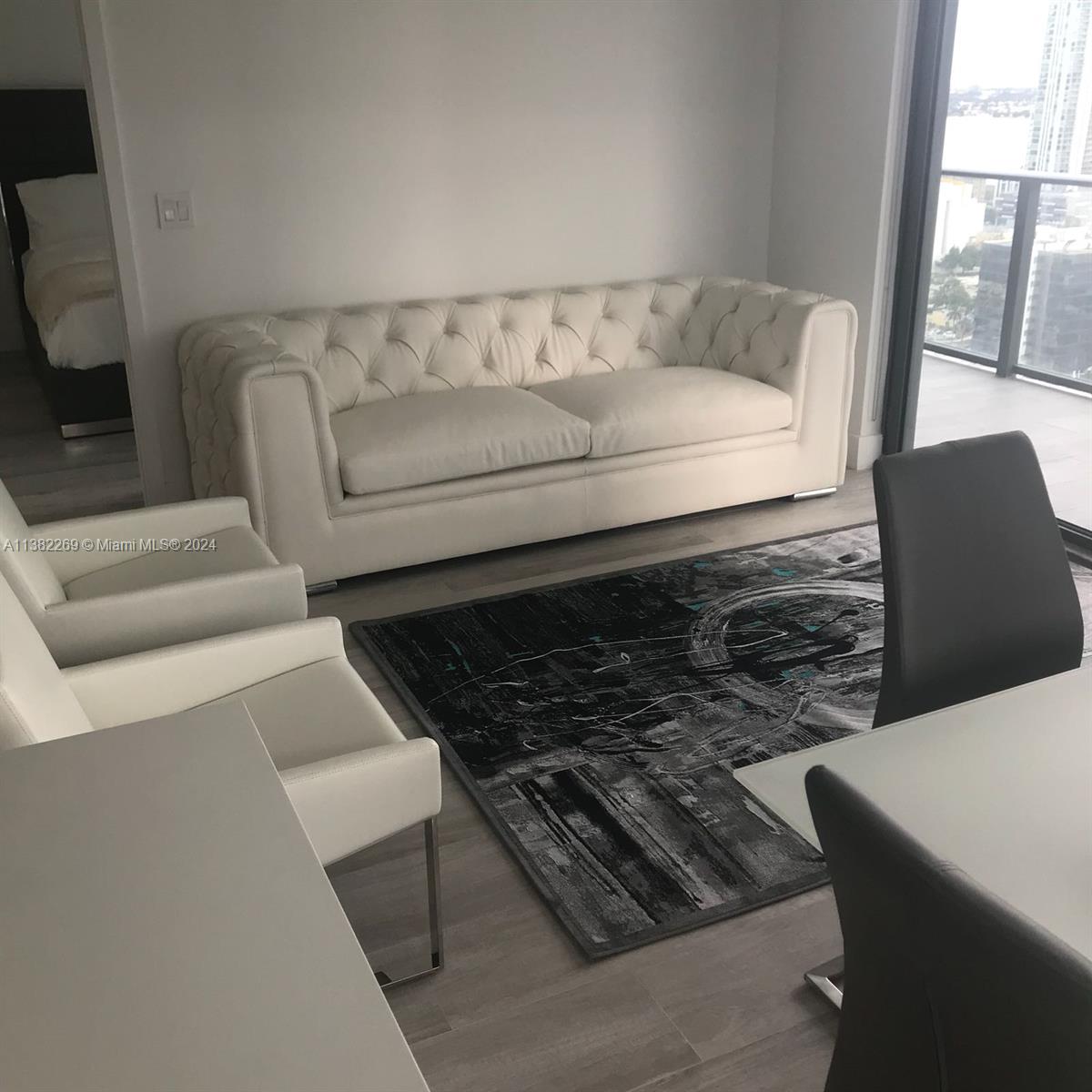 A modern living room features a white tufted sofa, two white chairs, and an abstract rug — 121 NE 34th St # 2601, Miami FL 33137, MIAMI, FL