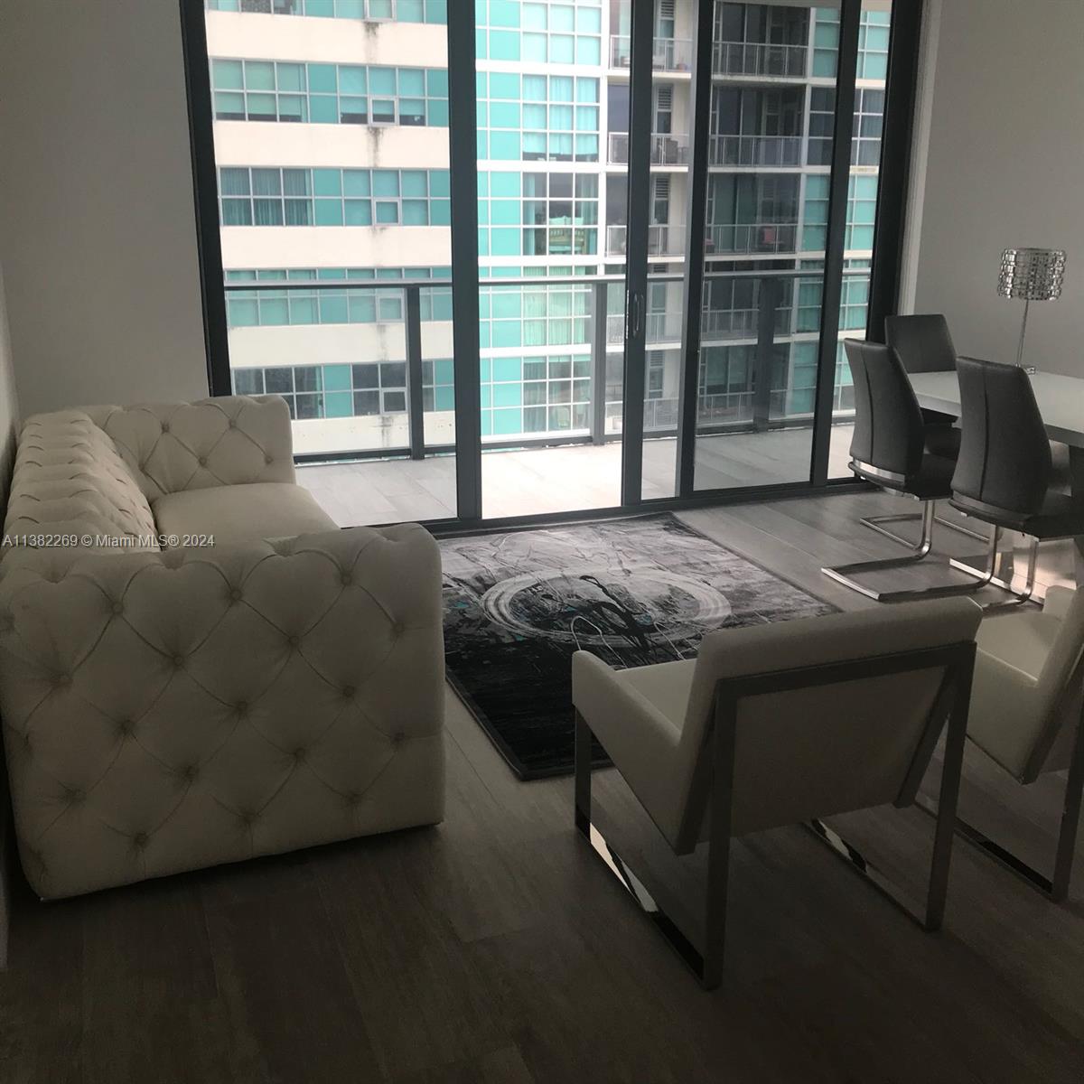 A living and dining area features a tufted sofa, modern chairs, and floor-to-ceiling windows — 121 NE 34th St # 2601, Miami FL 33137, MIAMI, FL