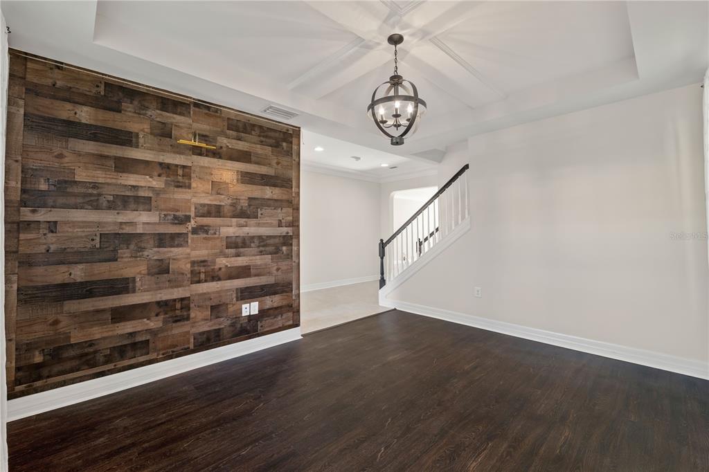 A dining room features a wood-plank accent wall, dark flooring, and a coffered ceiling — 4522 SCARLET LOOP, WESLEY CHAPEL, FL