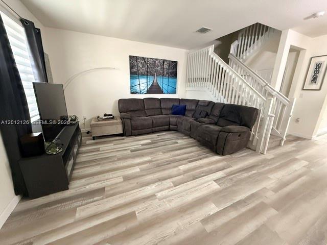 A living room features a gray sectional sofa, a television console, and light wood flooring — HIALEAH, FL