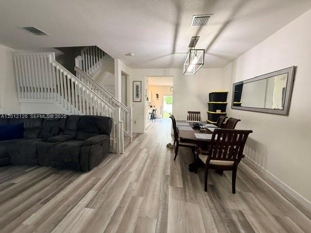 A living room and dining area feature light wood-look flooring and a staircase with railings — HIALEAH, FL