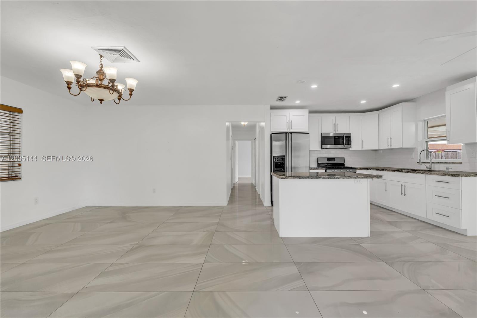 A kitchen with white cabinets and a granite island opens into a tiled dining area — 9982 SW 196th St, Cutler Bay FL 33157, CUTLER BAY, FL