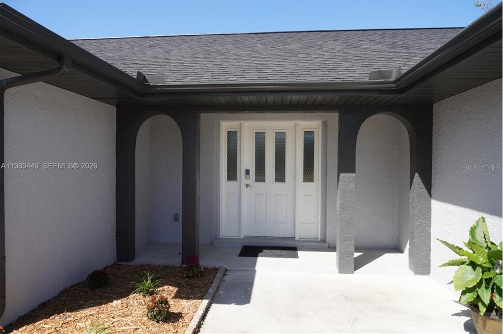 The exterior view shows a white front door with sidelights framed by two dark arches — 563 PRESQUE ISLE DRIVE, PORT CHARLOTTE, FL
