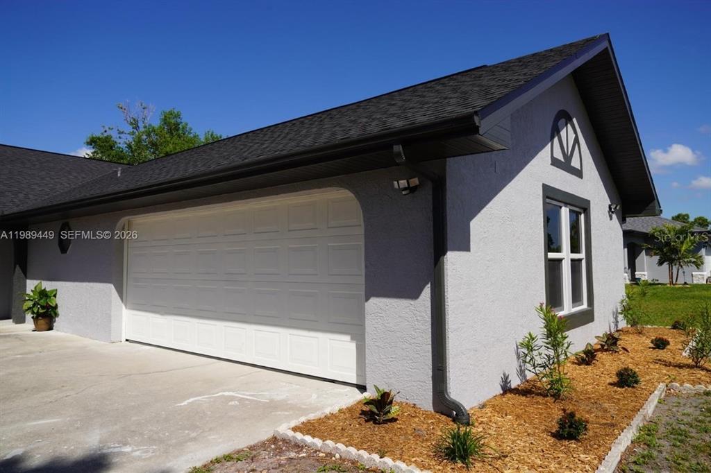 A gray stucco house exterior features a white two-car garage door and a side window — 563 PRESQUE ISLE DRIVE, PORT CHARLOTTE, FL
